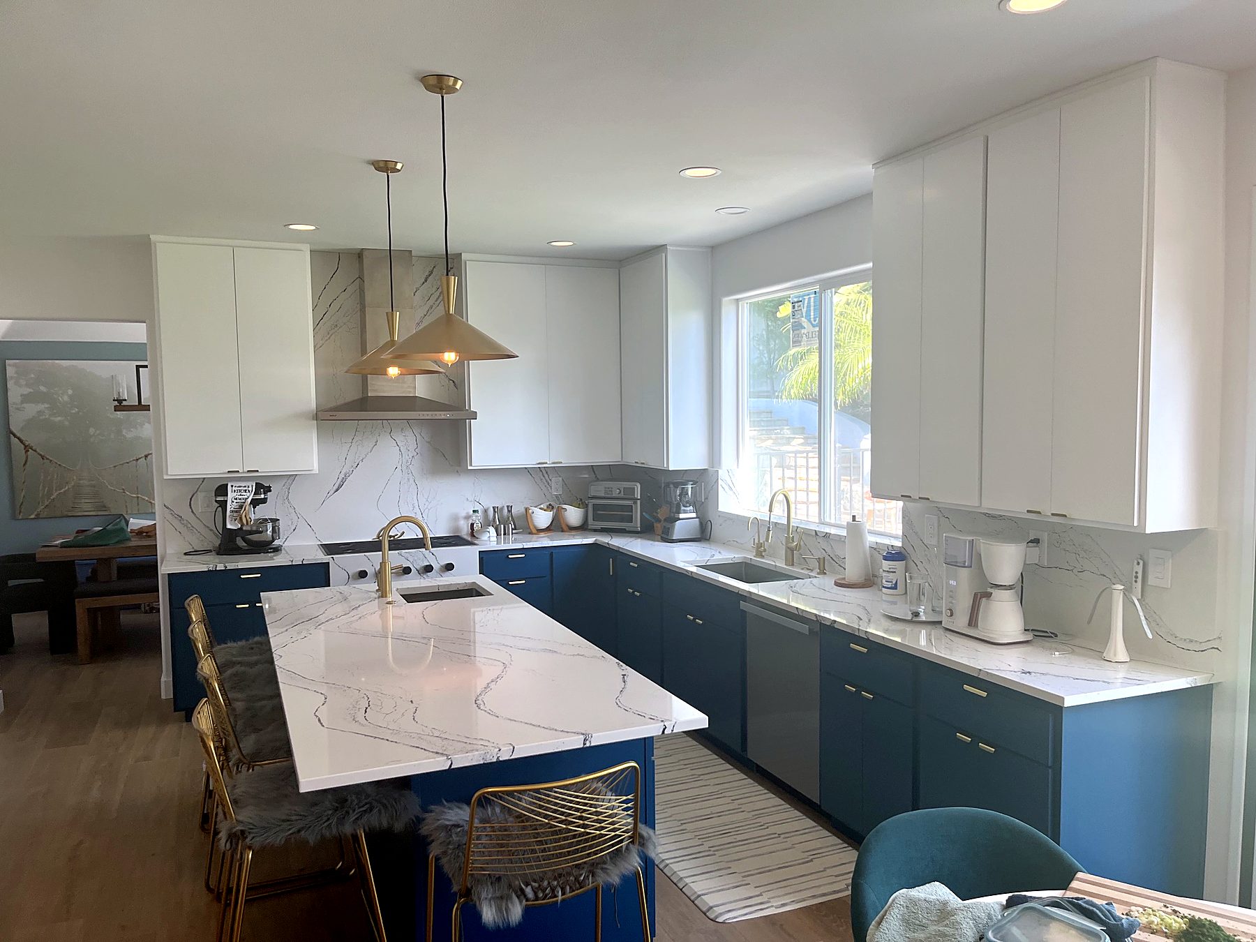 Finished kitchen with blue lower cabinets, white uppers, marble-look island and wood floors